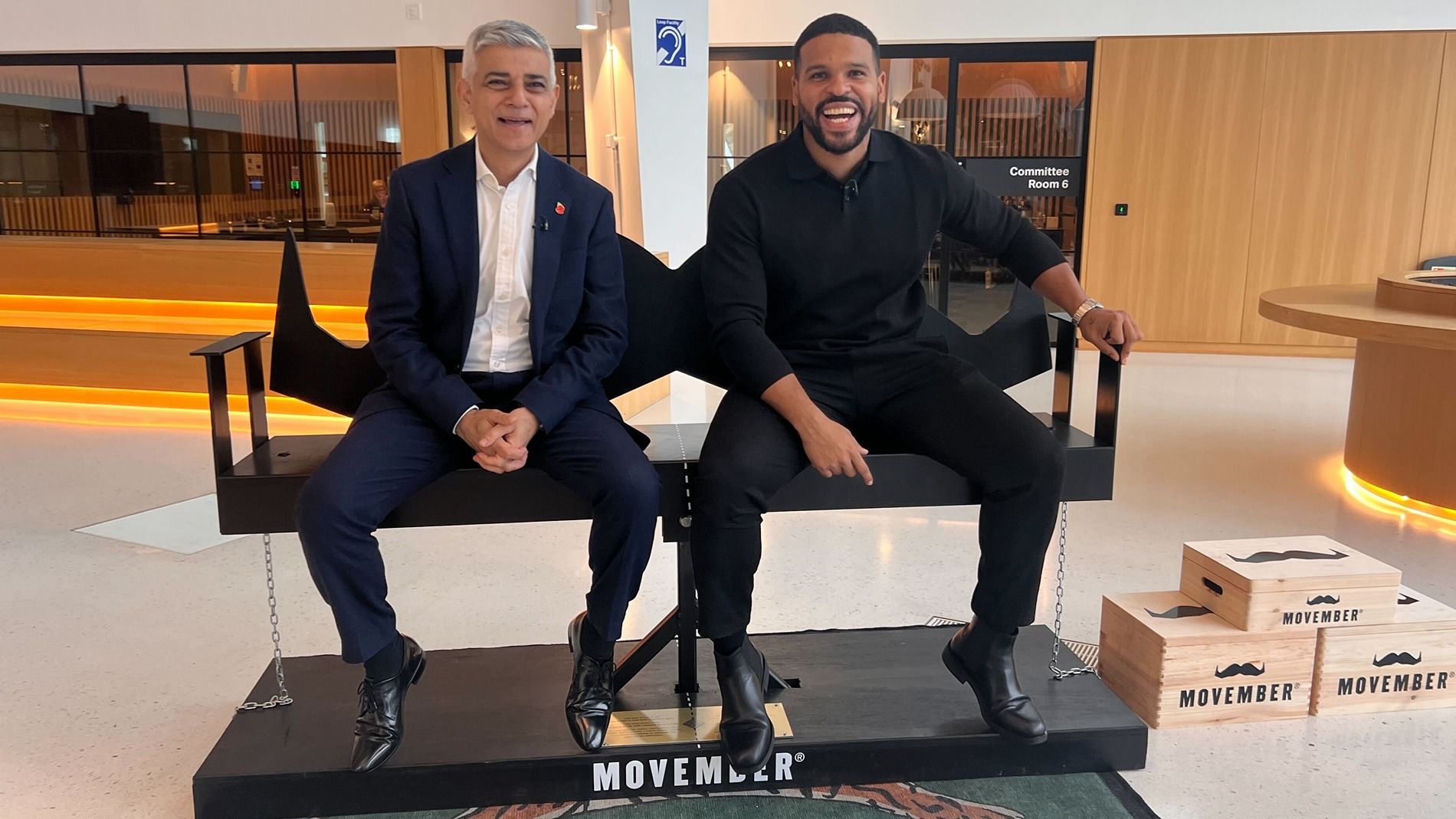 Photo of two people sitting on a moustache-shaped bench.