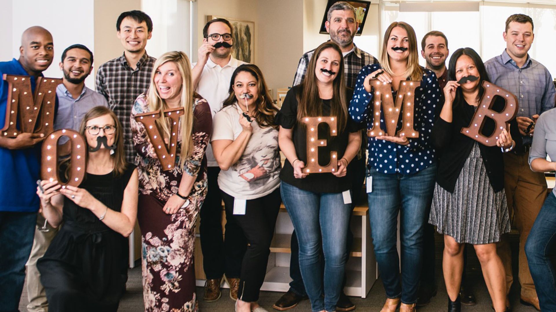 Photo showing smiling, enthusiastic officer workers, supporting Movember.