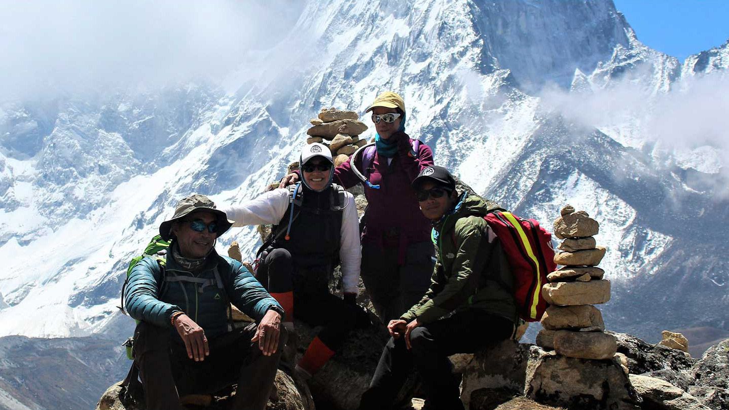 Photo of mountain climbers posing in front of breath-taking mountainous landscape.